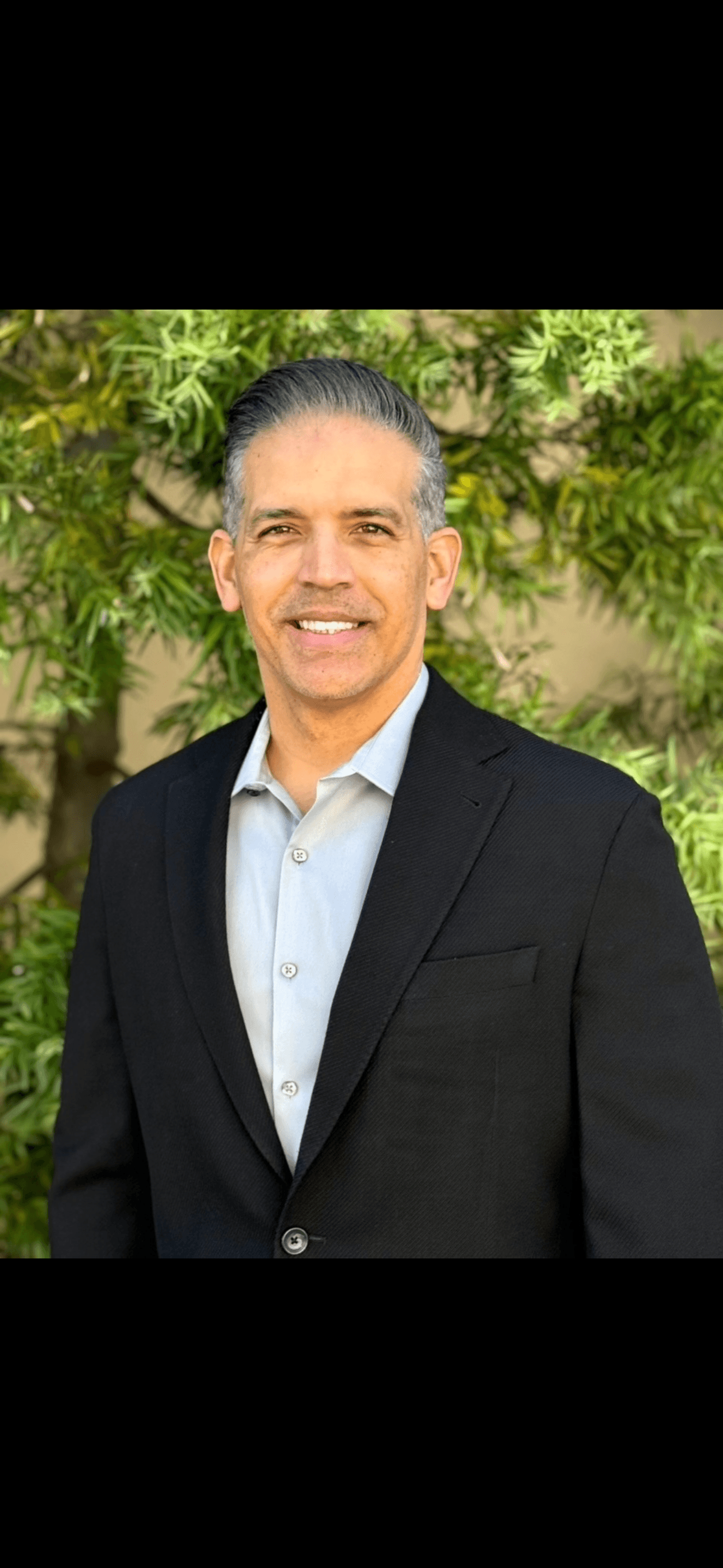 Smiling middle-aged man with salt-and-pepper hair wearing a black blazer and light blue shirt.